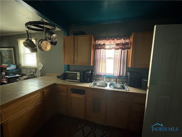 kitchen featuring tile countertops, a peninsula, crown molding, and a sink