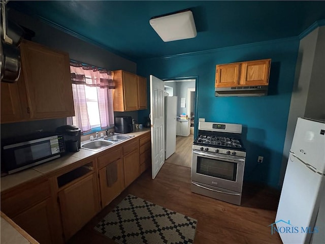 kitchen with tile countertops, a sink, dark wood-type flooring, under cabinet range hood, and appliances with stainless steel finishes