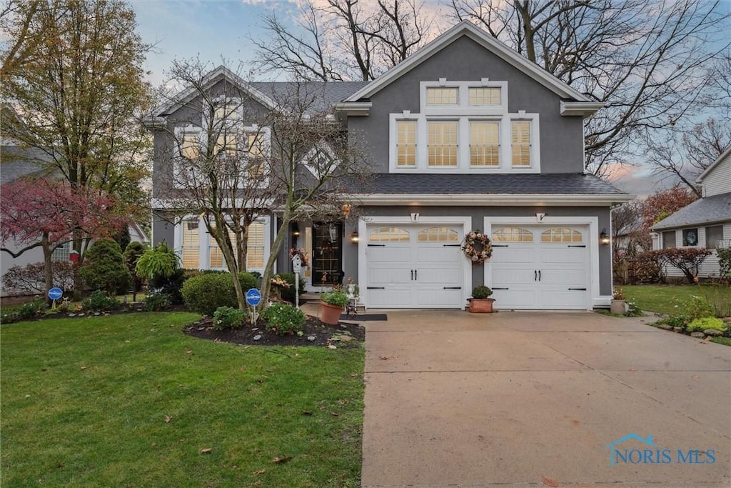 traditional-style home featuring a garage, concrete driveway, a front lawn, and stucco siding