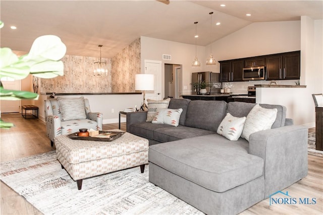 living area with baseboards, high vaulted ceiling, an inviting chandelier, light wood-style flooring, and recessed lighting
