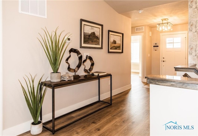 entrance foyer with visible vents, baseboards, wood finished floors, and a chandelier