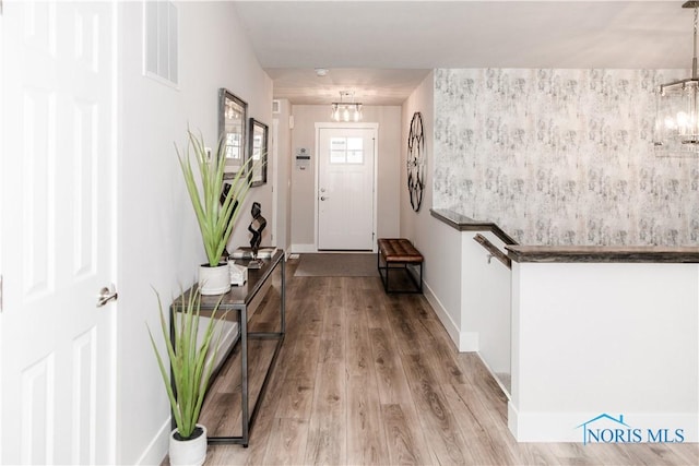 entrance foyer with visible vents, baseboards, an inviting chandelier, and wood finished floors