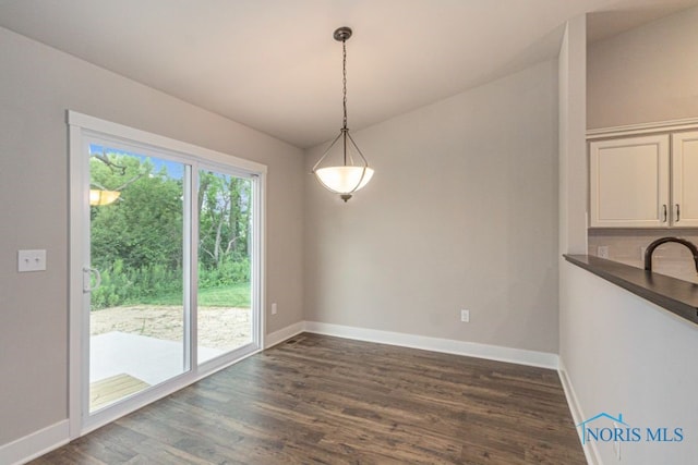 unfurnished dining area featuring baseboards and dark wood-type flooring