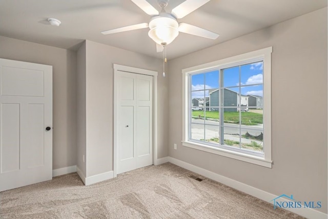 unfurnished bedroom featuring visible vents, baseboards, light carpet, a closet, and a ceiling fan