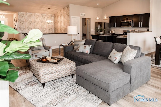 living room with visible vents, baseboards, an inviting chandelier, and light wood finished floors