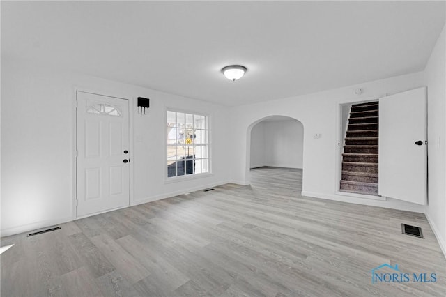 entryway with arched walkways, visible vents, stairs, and wood finished floors