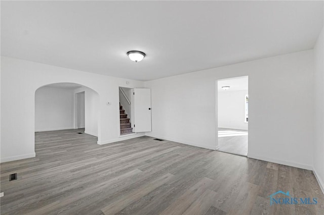 spare room with wood finished floors, visible vents, baseboards, arched walkways, and stairs