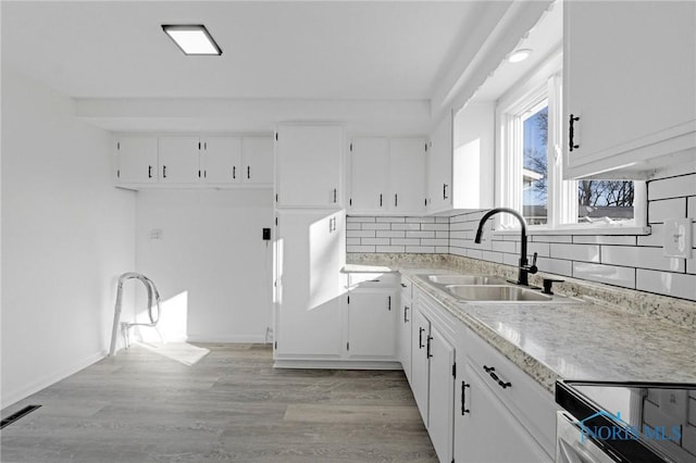 kitchen with light wood-type flooring, light countertops, decorative backsplash, white cabinetry, and a sink