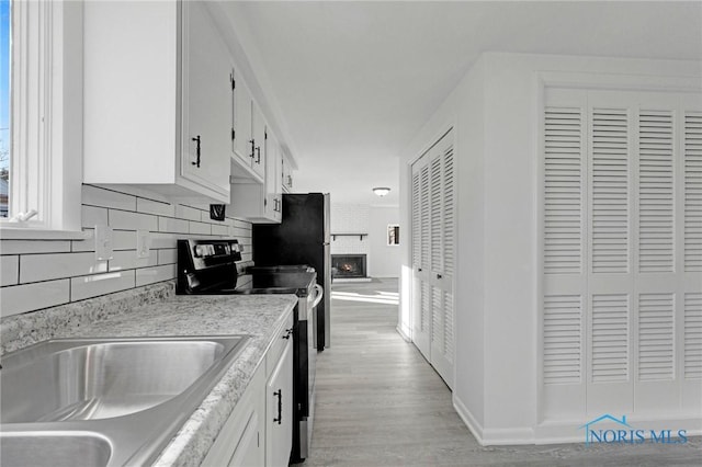 kitchen featuring stainless steel electric range oven, light wood finished floors, a sink, white cabinetry, and backsplash