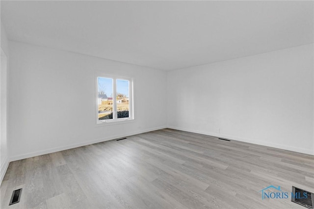 spare room featuring wood finished floors, visible vents, and baseboards