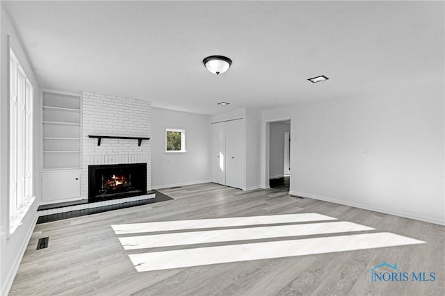 unfurnished living room featuring visible vents, a fireplace, baseboards, and wood finished floors