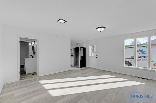 unfurnished living room featuring light wood finished floors, visible vents, and baseboards