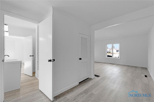 hallway with a sink, baseboards, and light wood-style flooring