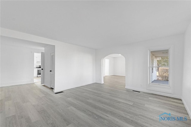 unfurnished room with visible vents, arched walkways, baseboards, and light wood-style flooring