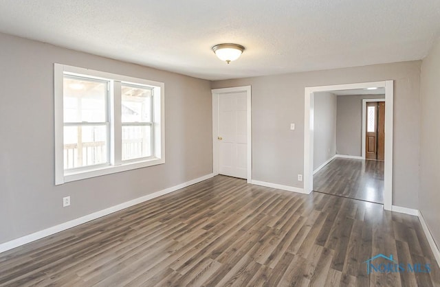 unfurnished room with baseboards, a textured ceiling, and dark wood finished floors