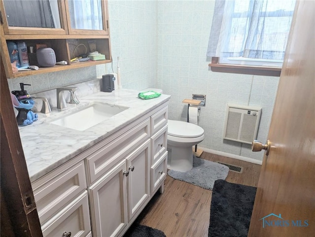 bathroom with visible vents, tile walls, toilet, wood finished floors, and vanity