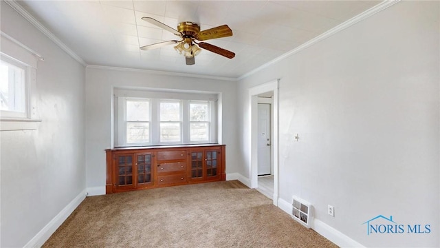 carpeted empty room featuring crown molding, visible vents, a ceiling fan, and baseboards