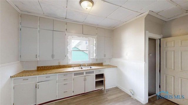 kitchen featuring a sink, a wainscoted wall, light wood finished floors, light countertops, and white cabinetry