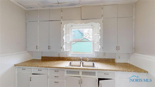 kitchen with a wainscoted wall, a sink, and light countertops