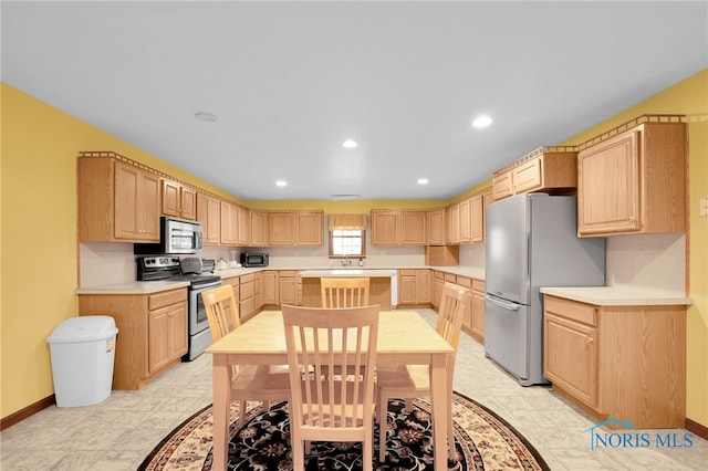 kitchen featuring light brown cabinetry, stainless steel appliances, light countertops, and baseboards