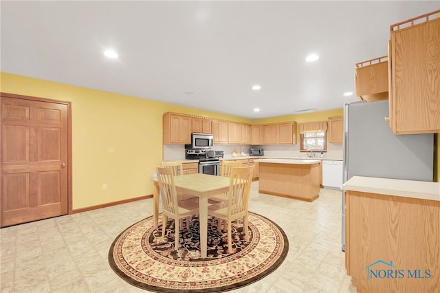 kitchen with light brown cabinetry, a center island, stainless steel appliances, and light countertops