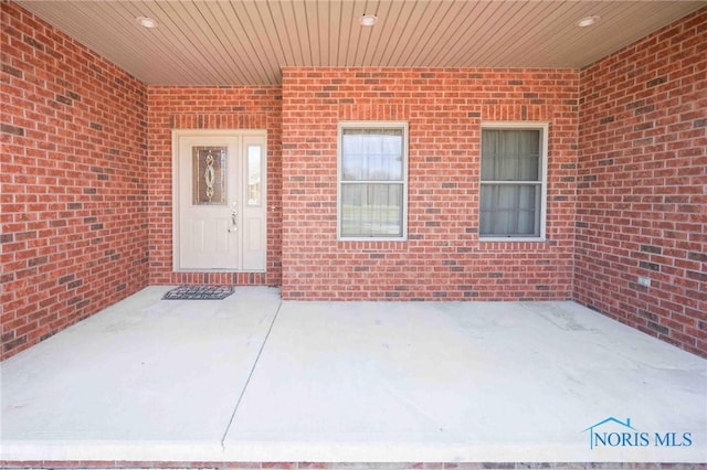 view of exterior entry with a patio area and brick siding