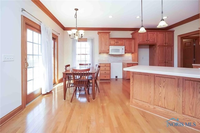 kitchen featuring a notable chandelier, hanging light fixtures, white microwave, light wood-style flooring, and ornamental molding
