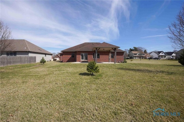 rear view of house featuring a yard, brick siding, and fence