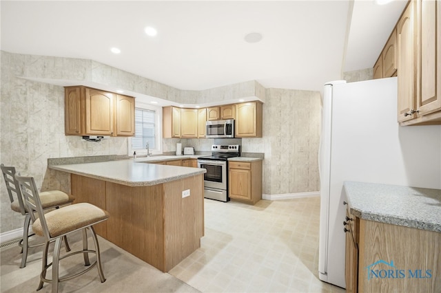 kitchen with light countertops, a peninsula, baseboards, appliances with stainless steel finishes, and a breakfast bar area