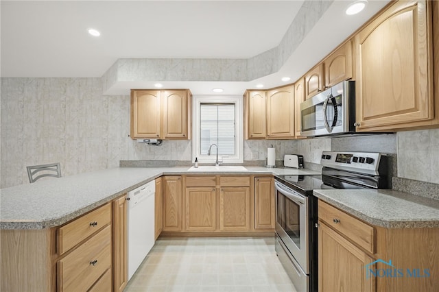 kitchen featuring a sink, light brown cabinetry, appliances with stainless steel finishes, a peninsula, and decorative backsplash