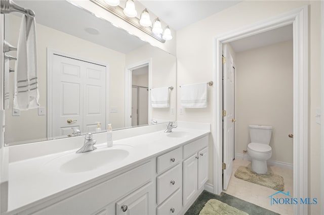 bathroom featuring toilet, a sink, double vanity, and baseboards