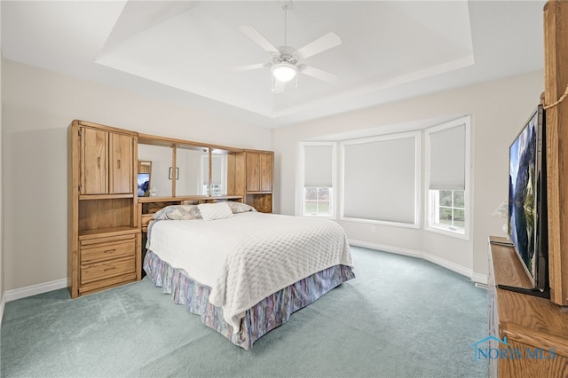 carpeted bedroom featuring baseboards, ceiling fan, and a raised ceiling