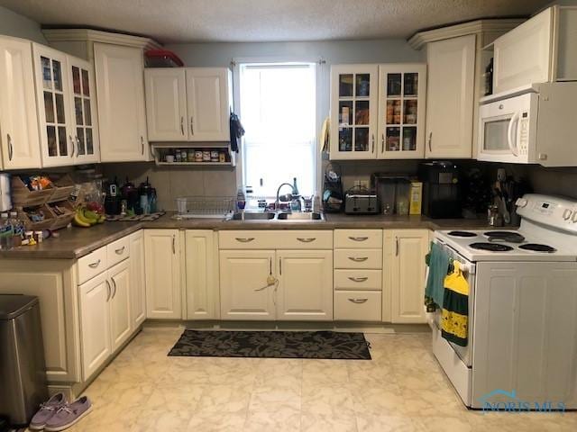 kitchen featuring a sink, dark countertops, glass insert cabinets, and white appliances