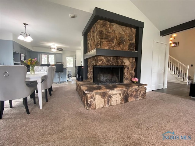 living area featuring vaulted ceiling, stairs, carpet flooring, ceiling fan with notable chandelier, and a fireplace