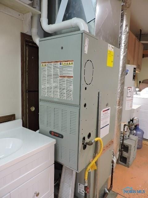utility room with water heater, heating unit, and a sink