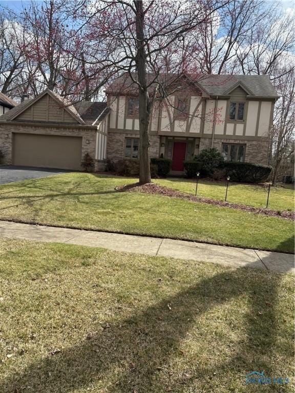 english style home with stucco siding, a front yard, a garage, and aphalt driveway