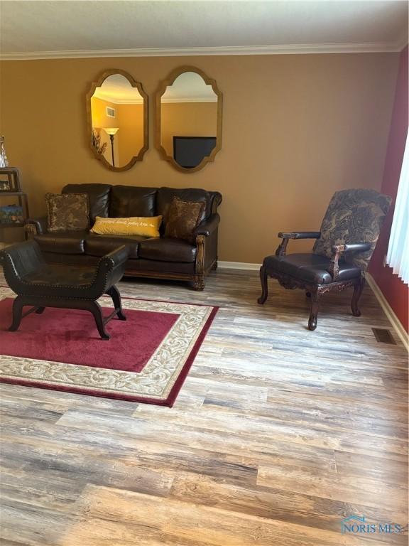 living area with baseboards, visible vents, wood finished floors, and ornamental molding
