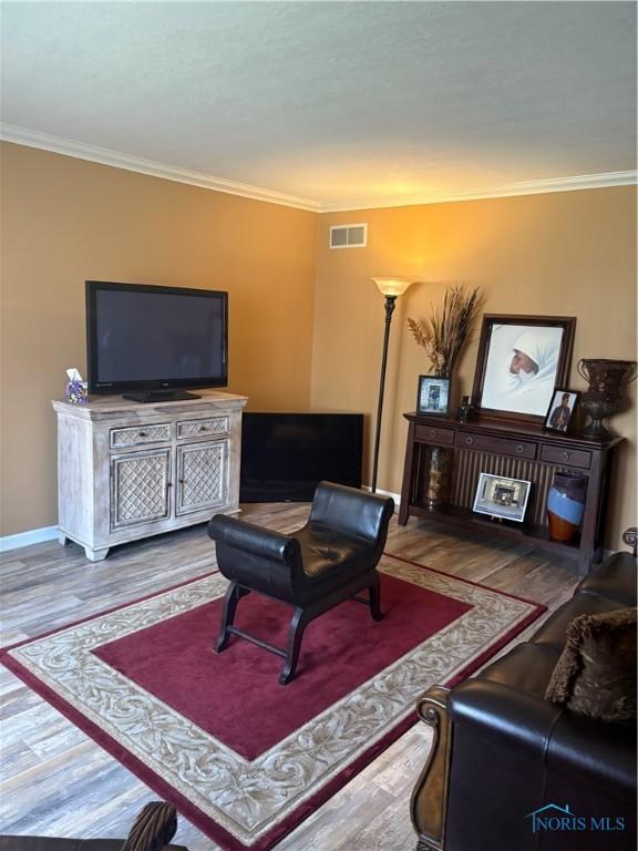 living room featuring wood finished floors, ornamental molding, baseboards, and visible vents