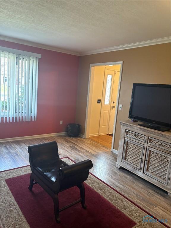 living area featuring baseboards, crown molding, and wood finished floors
