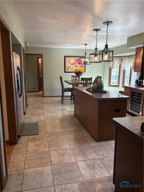 kitchen featuring visible vents, dark countertops, a kitchen island, beverage cooler, and hanging light fixtures