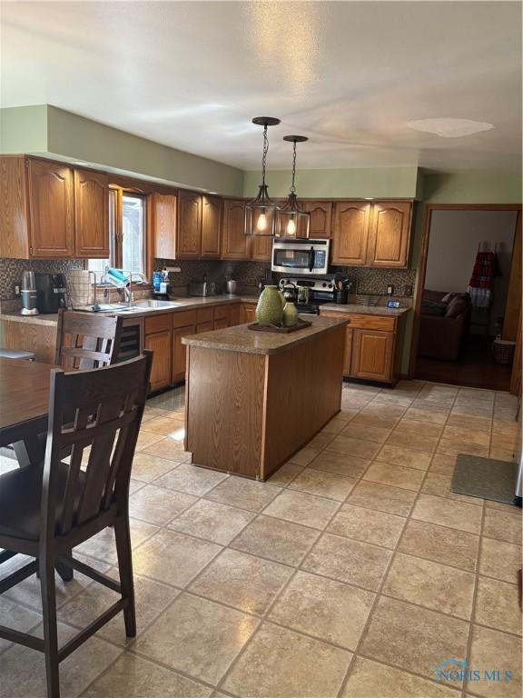 kitchen featuring decorative backsplash, brown cabinetry, stainless steel microwave, and a center island