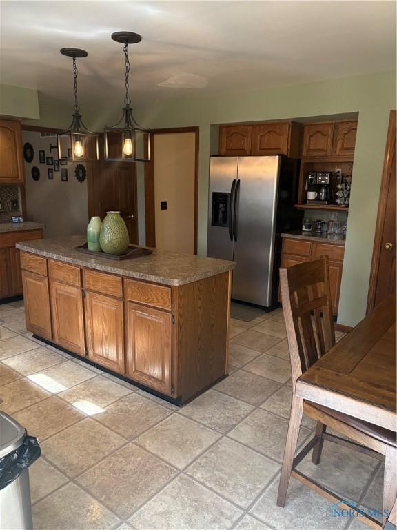 kitchen featuring a kitchen island, brown cabinetry, stainless steel refrigerator with ice dispenser, decorative light fixtures, and decorative backsplash