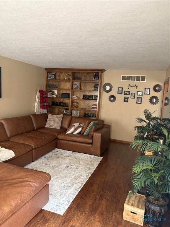 living room featuring baseboards, visible vents, wood finished floors, and a textured ceiling