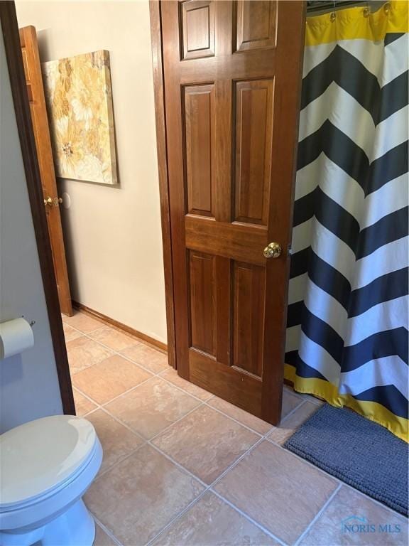 bathroom with a shower with curtain, tile patterned floors, toilet, and baseboards