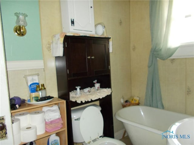 full bath with tile walls, toilet, and a soaking tub