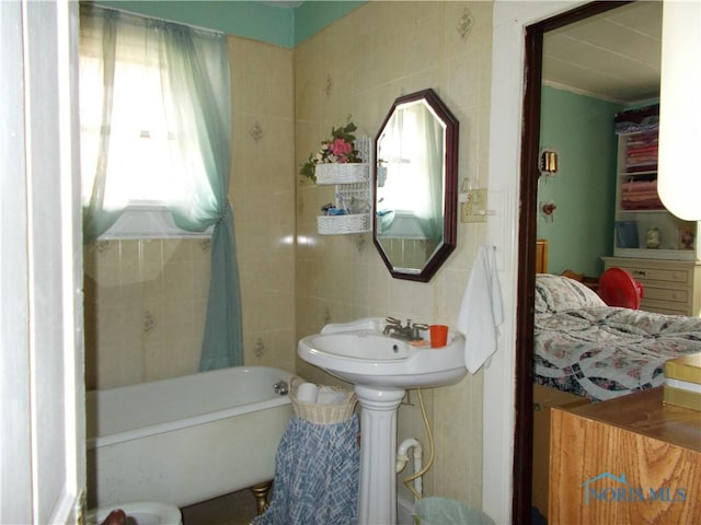 full bath featuring a sink, a tub to relax in, and tile walls