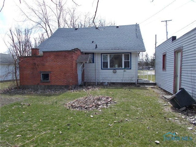 back of property with a shingled roof and a lawn