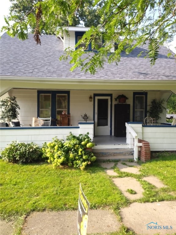 entrance to property featuring a yard, covered porch, and roof with shingles