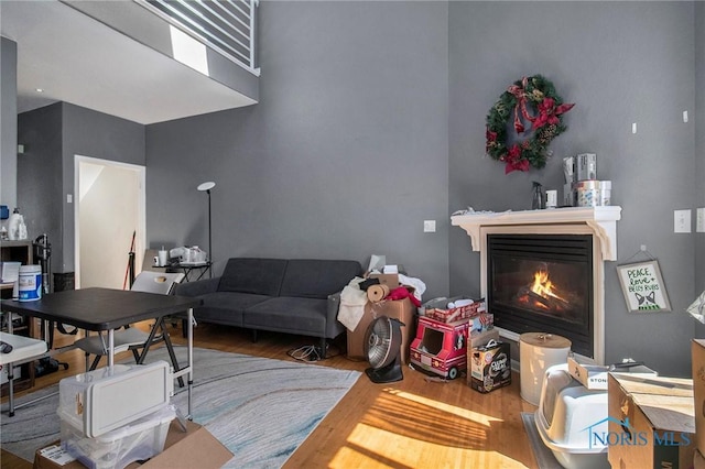 living area with a high ceiling, wood finished floors, and a glass covered fireplace