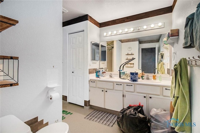 full bath featuring a textured wall, double vanity, a sink, and toilet